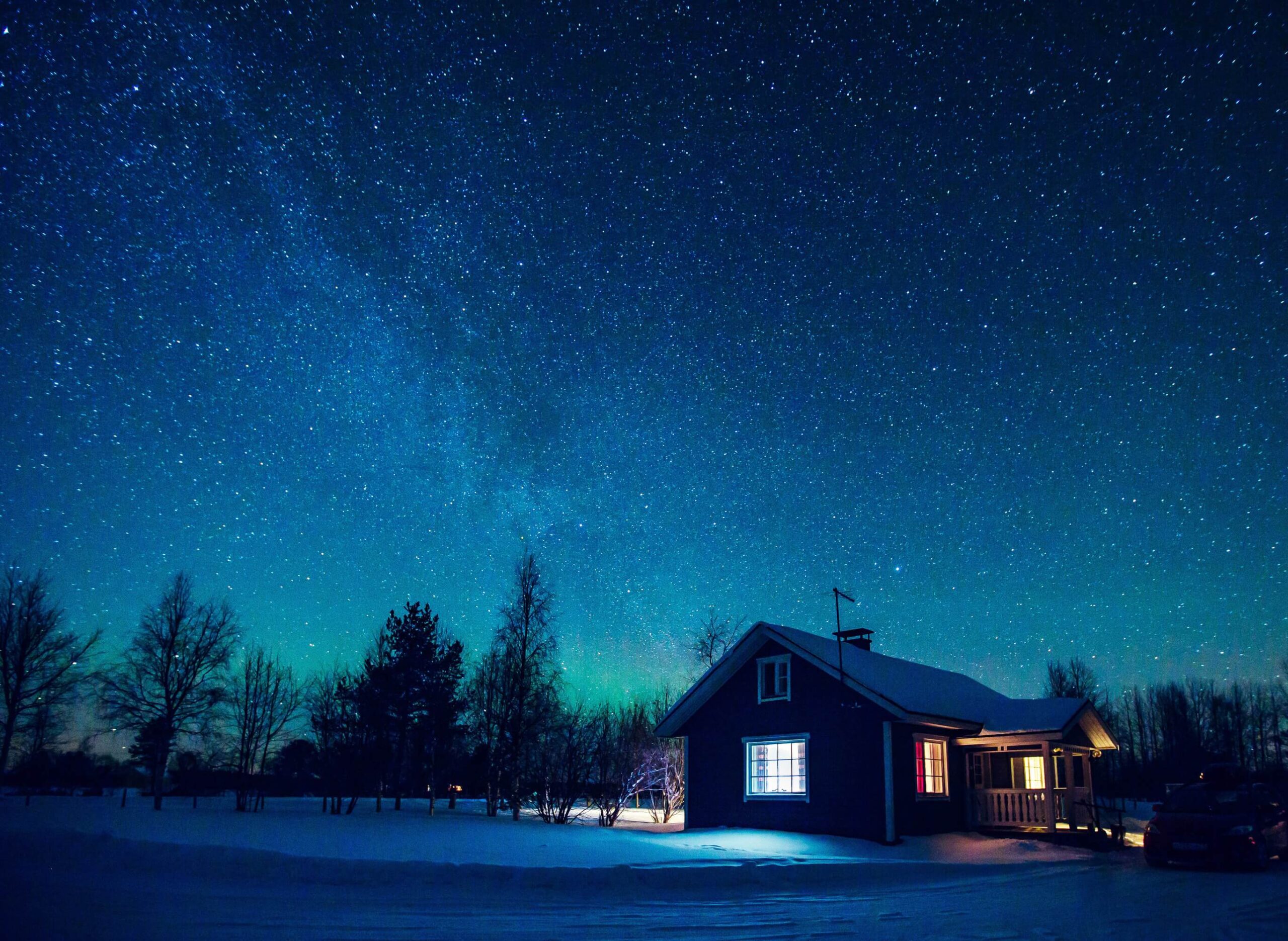 Talvinen tähtimaisema ja taustalla omakotitalo, josta valoa näkyy ikkunoista.