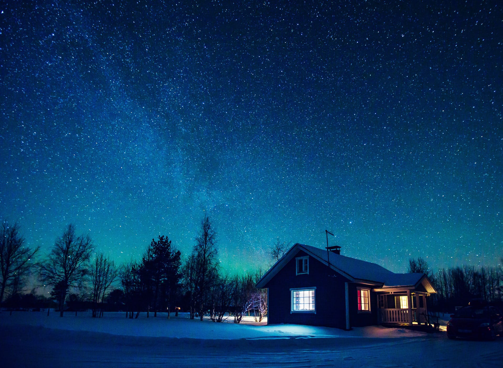 Talvinen tähtimaisema ja taustalla talo, josta valoa näkyy ikkunoista.