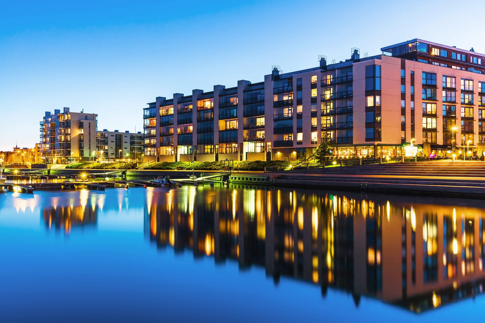 Kerrostalo hämärässä ja talo heijastuu edessä olevaan veteen.