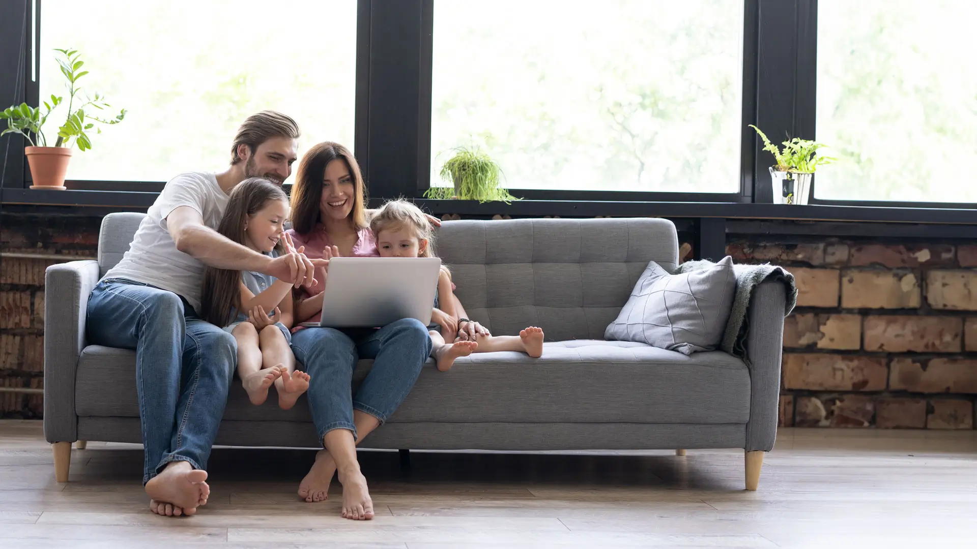 Nelihenkinen perhe istumassa sohvalla katsomassa tietokonetta yhdessä.
