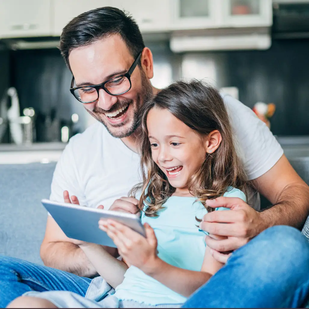Mies ja lapsi istuvat sohvalla katsomassa tablettia yhdessä.