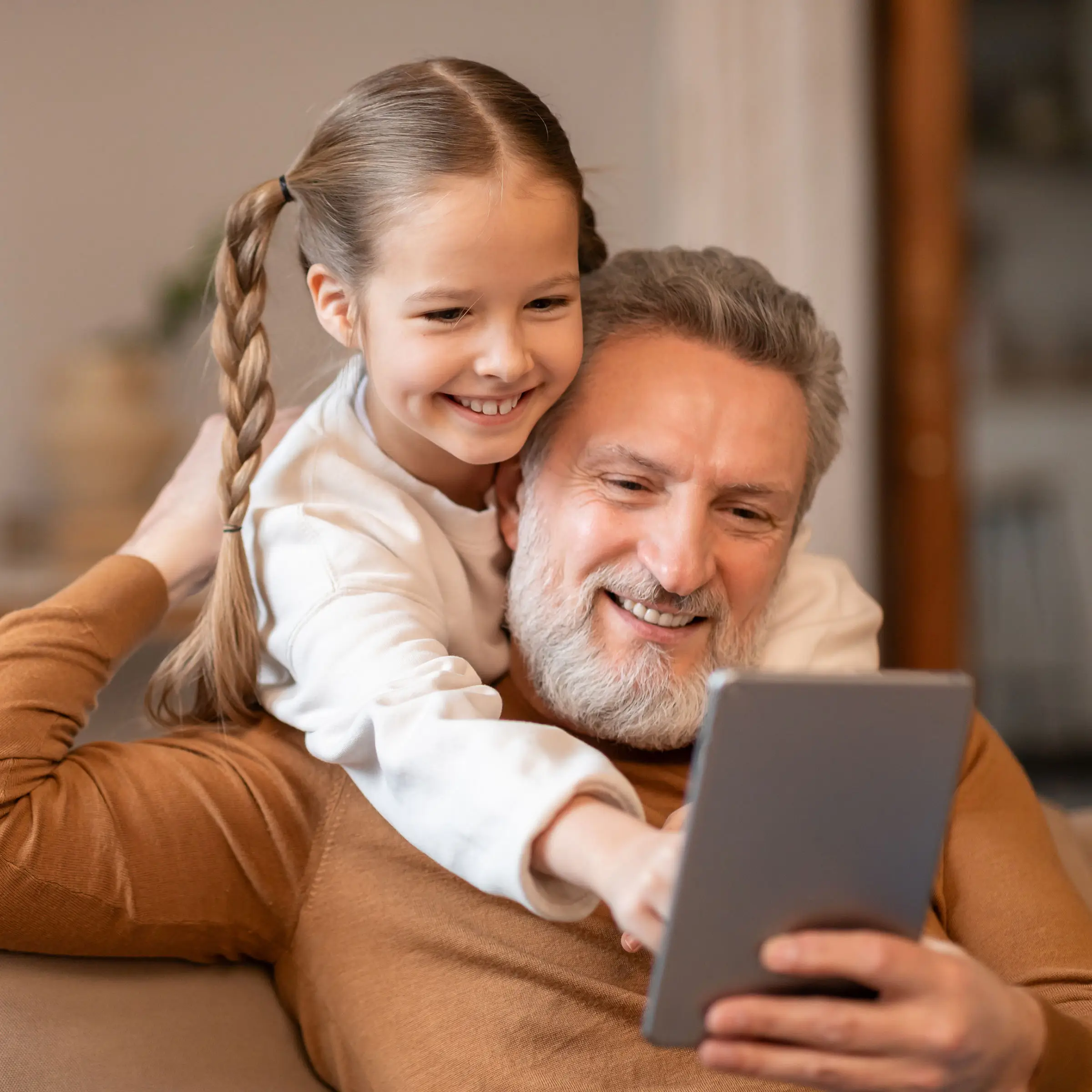 Vanhempi mies ja pieni tyttö katselevat hymyillen tablettia.