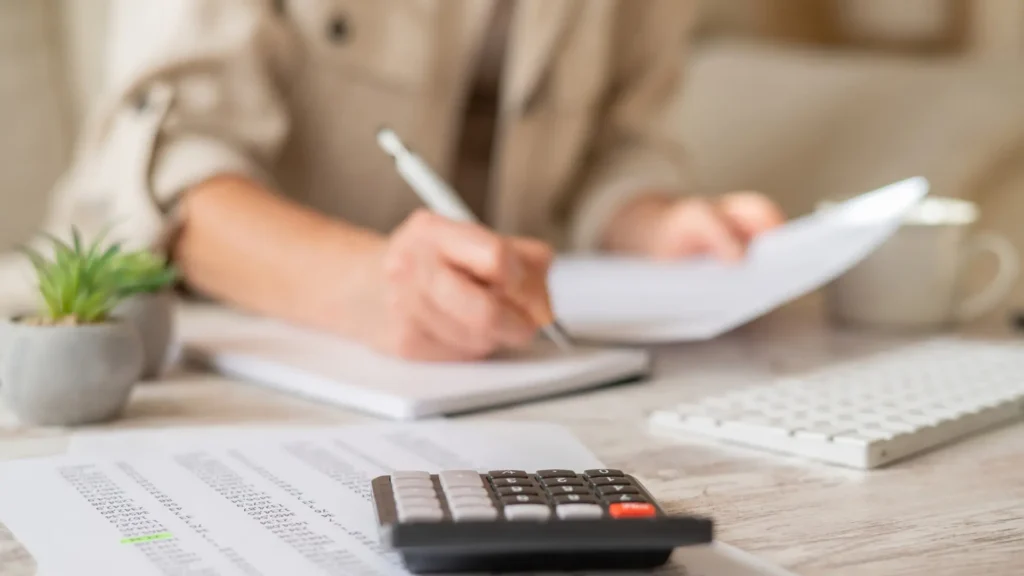 nainen laskee laskimella ja kirjoittaa muistivihkoon